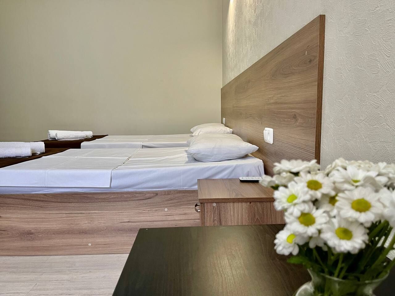 Un letto rifatto con lenzuola bianche e una testiera in legno, un piccolo tavolino laterale e un vaso con fiori bianchi.