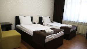 Habitación de hotel con dos camas, una mesita pequeña, una silla amarilla y una ventana con cortinas.