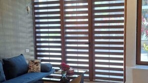 Una sala de estar moderna con un sofá, una mesa de centro y ventanas amplias con persianas.