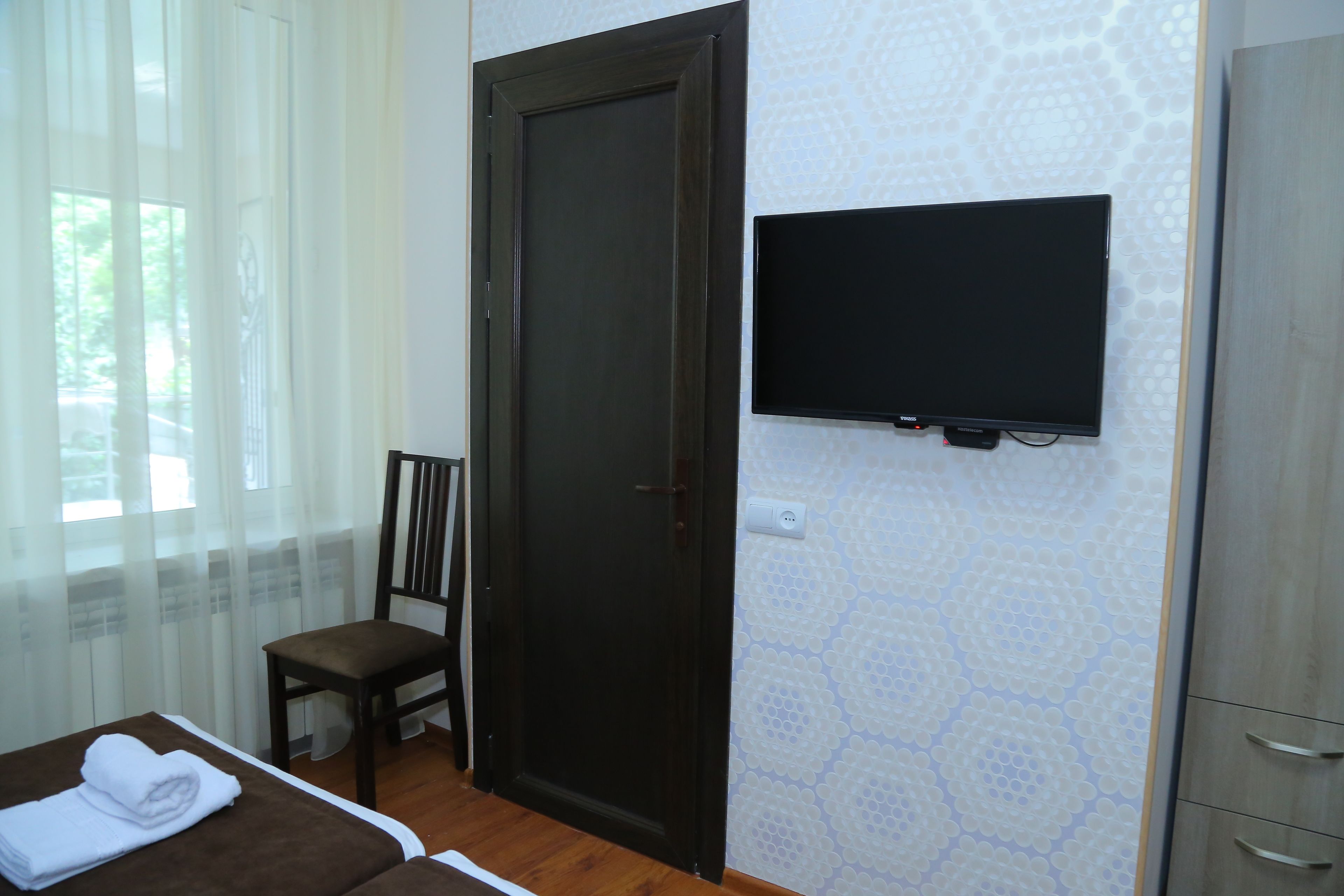 A hotel room with a bed, a chair, a TV mounted on the wall, and a wardrobe.