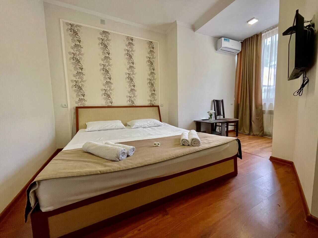 Un lit bien fait, agrémenté de serviettes pliées, une petite table avec une chaise et un appareil de climatisation fixé au mur.