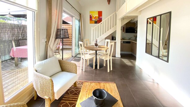 A spacious living area with a sofa, dining table, and chairs, a kitchen in the background, and a balcony with a table and chairs.