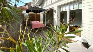 A patio with a table and chairs, a wooden deck, and a house with white siding and a garage door.