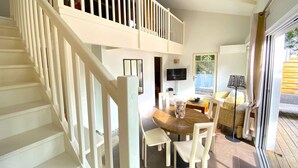 A dining area with a wooden table and chairs, a TV mounted on the wall, and a staircase with white railings leading to an upper level.