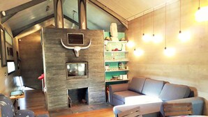 Ein gemütliches Wohnzimmer mit Kamin, einer Couch, einem Esstisch und einer Küchenzeile mit Regalen und Pendelleuchten.
