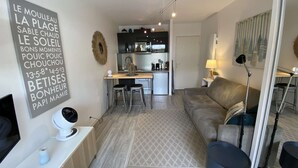 Ein modernes Wohnzimmer mit einer Couch, einem Essbereich mit Tisch und Stühlen, einer Küche im Hintergrund und einem dekorativen Wandbild.