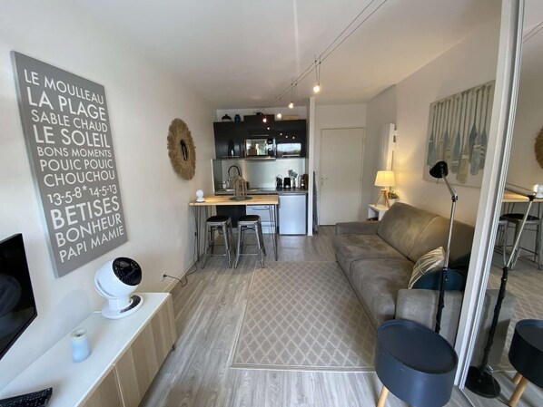 Ein modernes Wohnzimmer mit einer Couch, einem Essbereich mit Tisch und Stühlen, einer Küche im Hintergrund und einem dekorativen Wandbild.