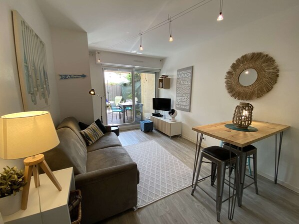 A modern living room with a sofa, a coffee table, and a TV. There is a dining area with a table and chairs.