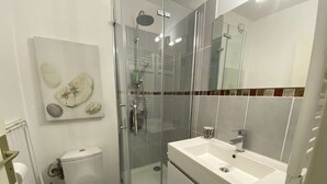 Ein modernes Badezimmer mit einer Duschkabine, einer weißen Toilette und einem geräumigen Waschtisch mit Spiegel.