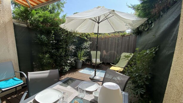 Eine Außenpatio mit Esstisch, Stühlen und einem großen Sonnenschirm.