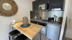 Eine kompakte Küche mit Holztisch, zwei Barhocker, einer Mikrowelle, einer Kaffeemaschine und einem Wasserkocher.