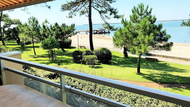Un balcon avec vue sur une plage, des arbres et une étendue d’eau.