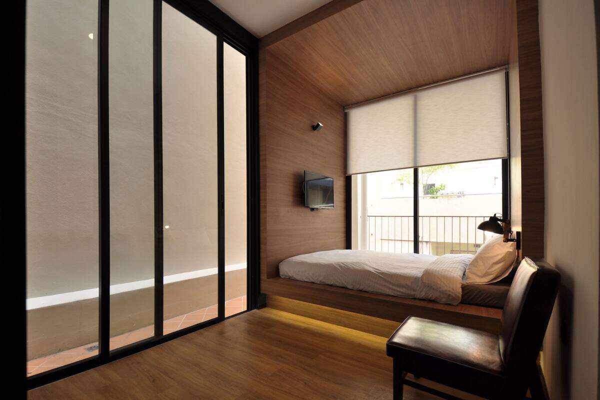 A modern bedroom with a large sliding glass door, a bed with a pillow, a chair, and a mounted TV.