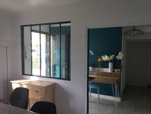 Een kamer met een houten bureau, een stoel, een spiegel, een vaas met bloemen en een blauwe accentmuur.