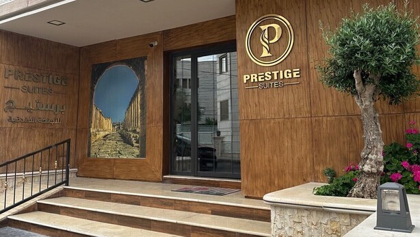 Entrada de un hotel con fachada de madera, un gran arco y un letrero que dice 'Prestige Suites'.