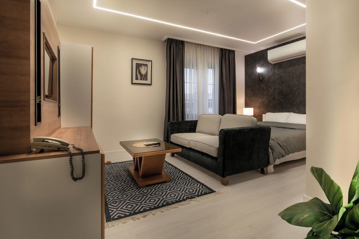 A modern hotel room with a sofa, a small table, a bed, and a plant.
