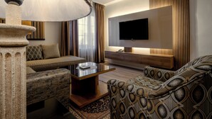 Una sala de estar moderna con un sofá, un sillón y una mesa de centro. Un televisor de pantalla plana está montado en la pared, y hay una lámpara decorativa.