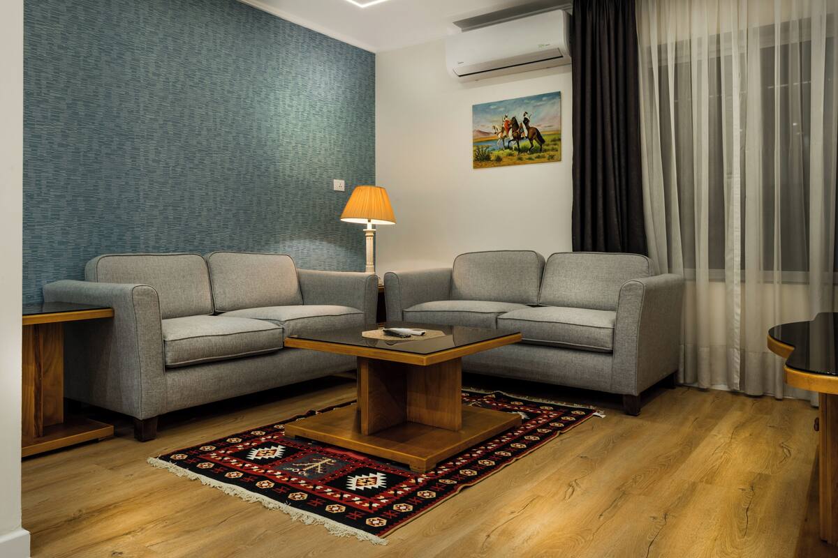 A modern living room with two grey sofas, a wooden coffee table, a patterned rug, and a painting on the wall.