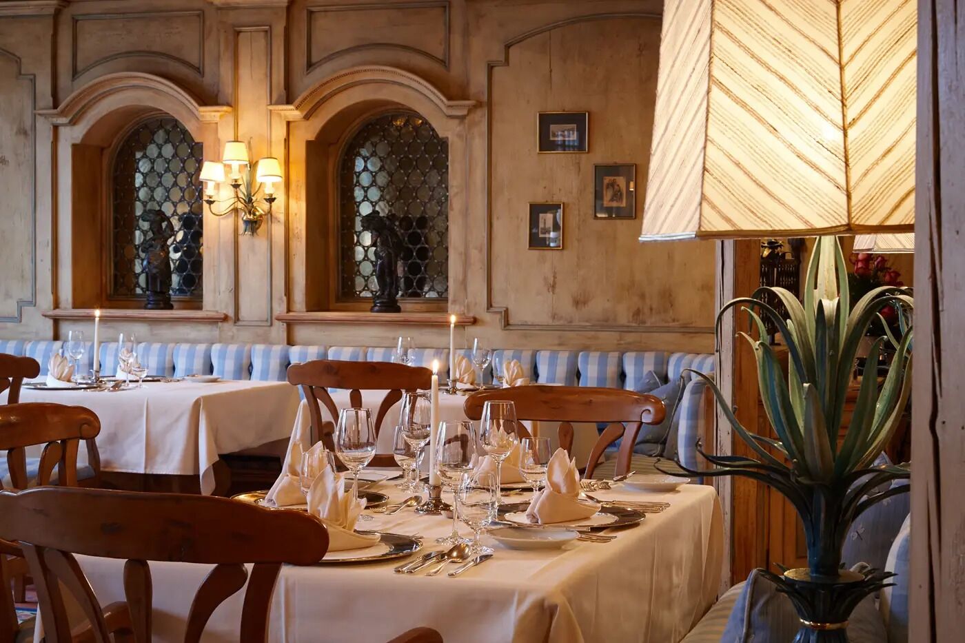 A restaurant with tables set for dining, featuring a classic interior with wooden paneling and arched windows.