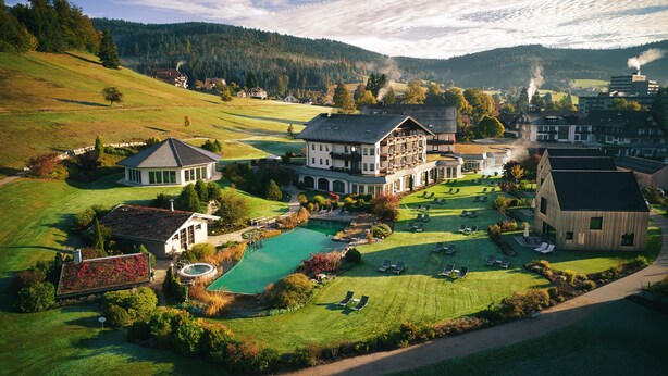 A large estate with a swimming pool, multiple buildings, and a mountainous backdrop.