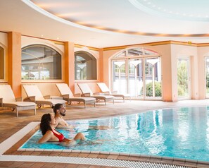 A pool area with lounge chairs and a glass-enclosed room with arched windows.