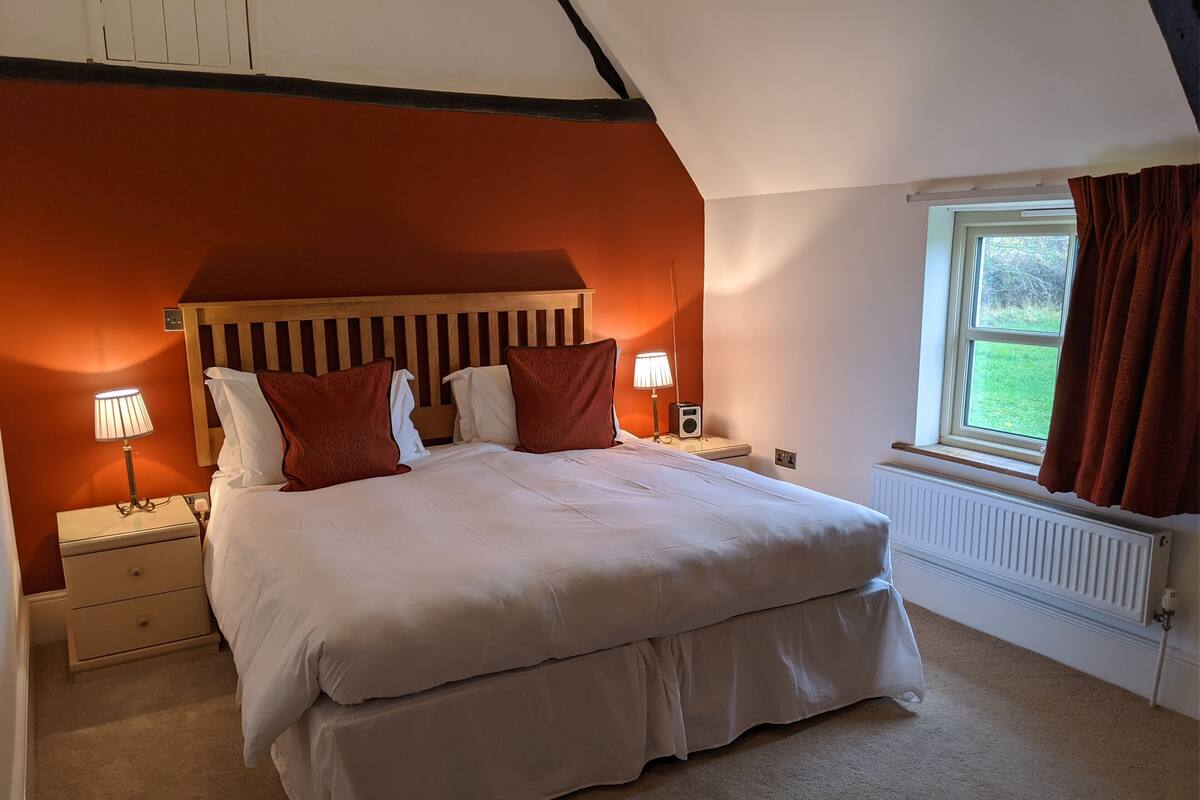 Ein Schlafzimmer mit einem großen Bett, zwei Nachttischen, einem Schrank und einem Fenster mit Vorhängen sowie einer Heizung.