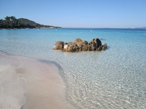 A beach with clear water, a rocky outcrop, and a distant hill.