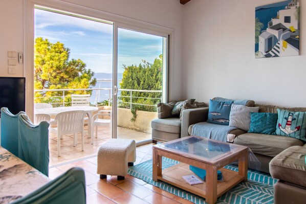 A living room with a sofa, a glass coffee table, and a view of the outdoors through a sliding glass door.