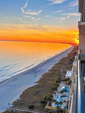 Un hotel frente al mar con vista a la playa y al océano al atardecer.