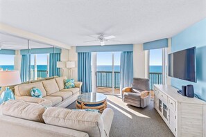 A modern hotel room with a balcony, a sofa, a chair, a TV, and a ceiling fan.