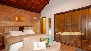 A bedroom with a large bed, a wooden headboard, a 'Love' sign on the wall, and a glass-enclosed bathroom with a bathtub. - Recanto das Acacias (Camanducaia)