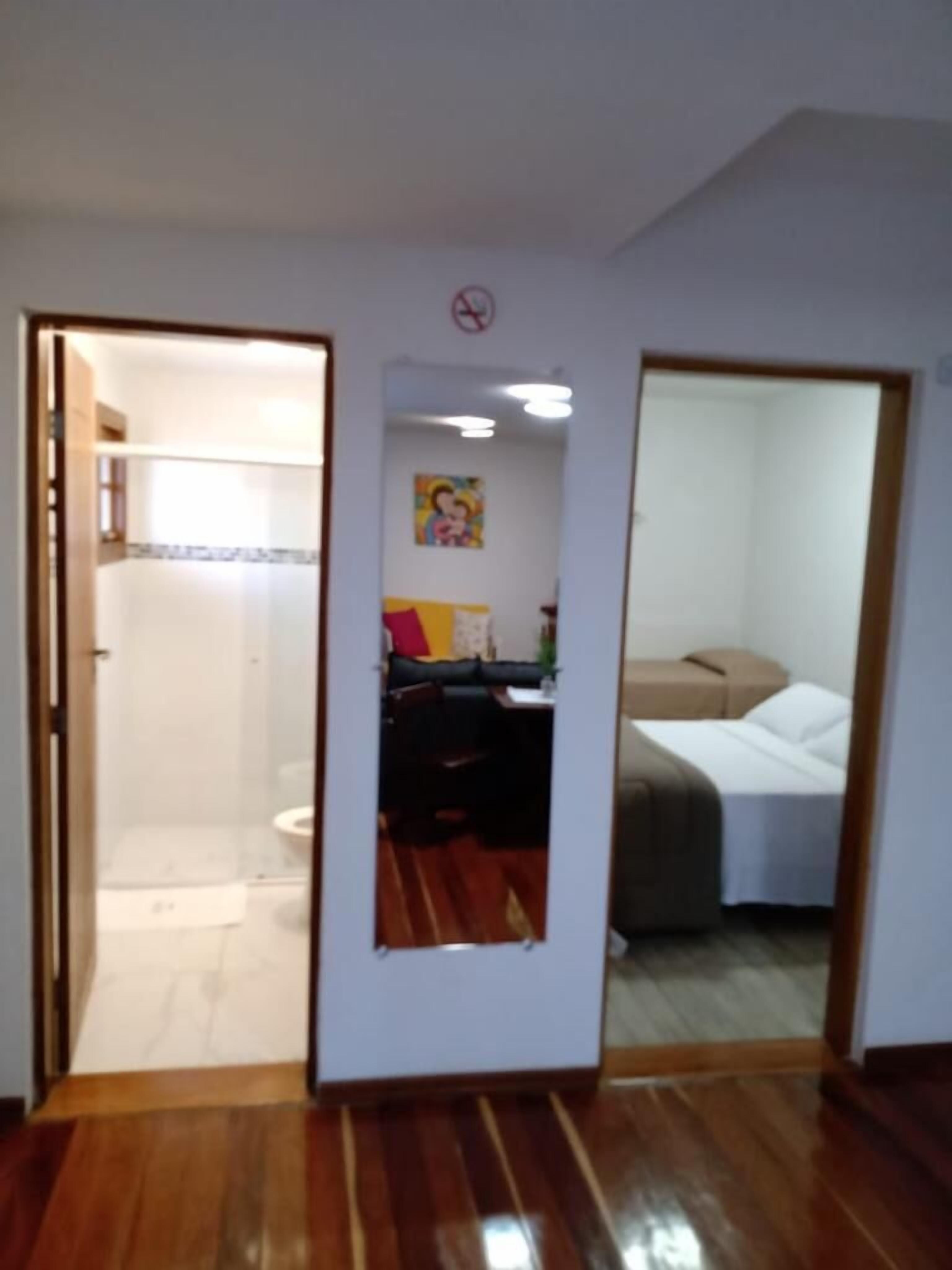 A room with a wooden floor, a bed, a desk, and a shower area.