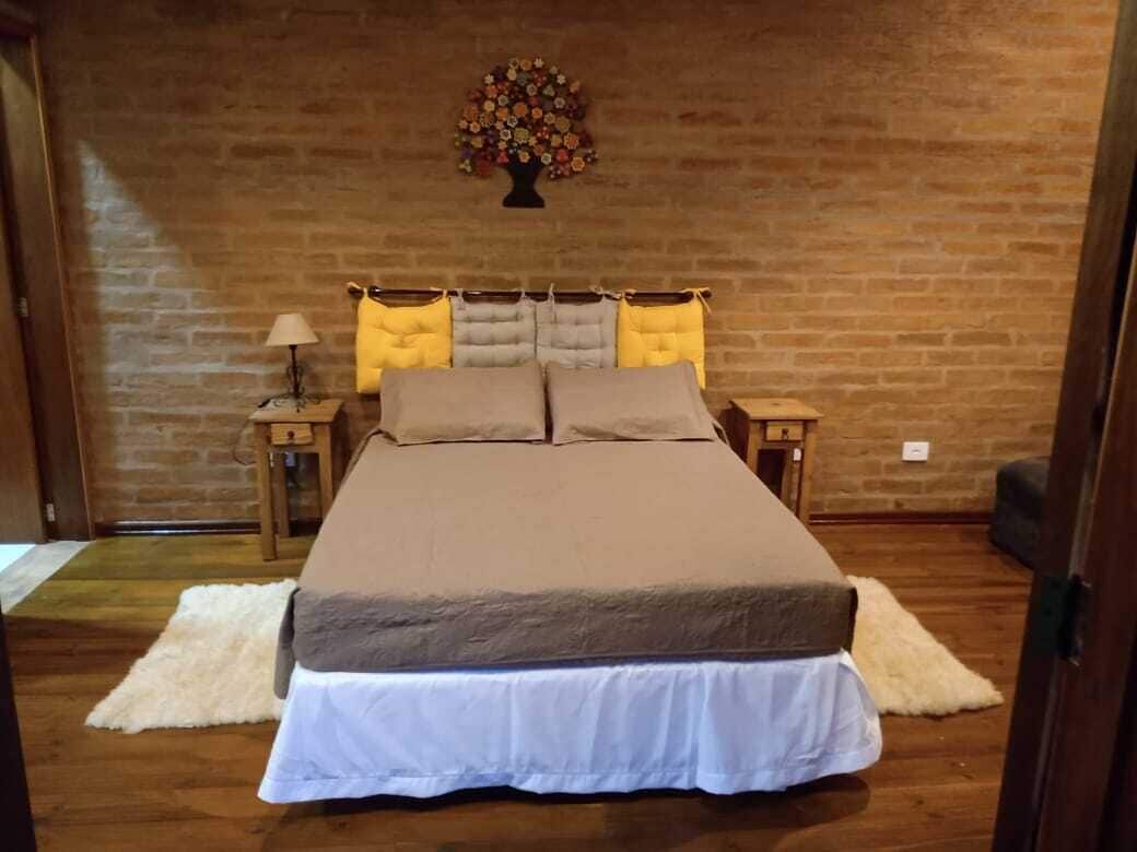 A bedroom with a brick wall, a bed with a white and brown bedspread, two nightstands with lamps, and a floral wall decoration.