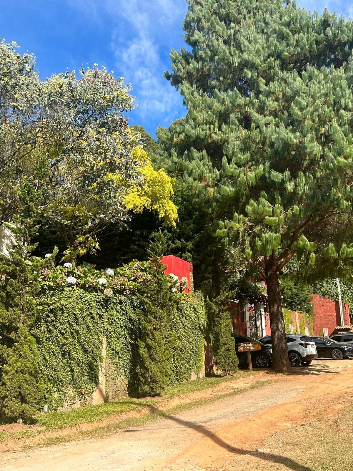 Un camino de tierra con coches estacionados y un edificio rojo al fondo.