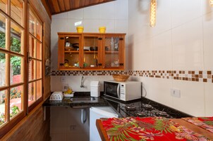 Una cocina con armarios de madera, microondas, fregadero y ventana con vistas al verdor.