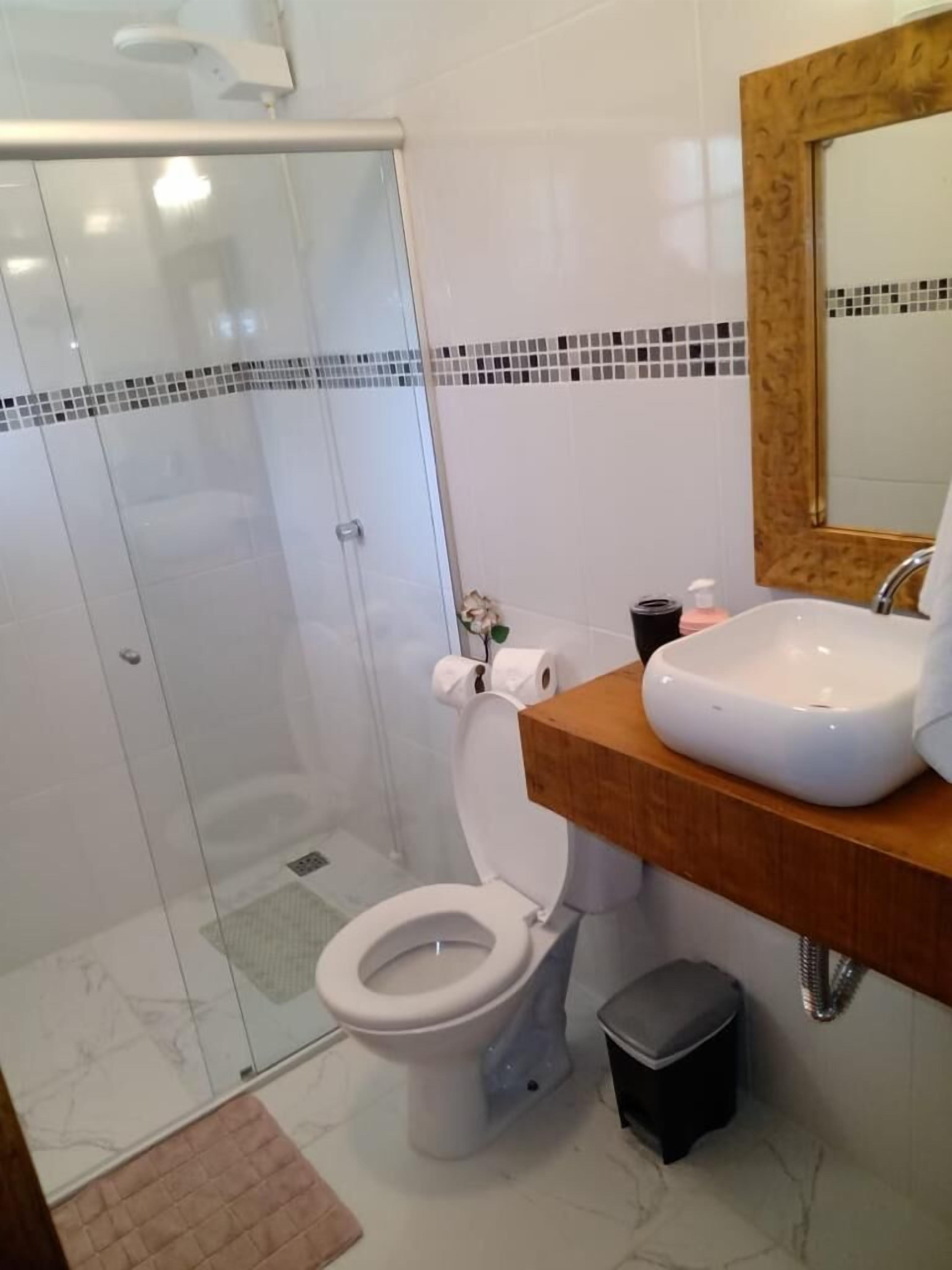 Une salle de bain moderne avec une douche à parois de verre, des toilettes blanches, un meuble-lavabo en bois et un miroir.