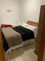 Una habitación pequeña con una cama individual, cabecera de madera, almohada roja y manta color beige.