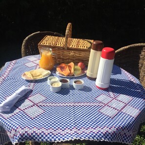 Montaje para un picnic con mantel a cuadros, una cesta de mimbre, jarras de jugo, un termo y diferentes alimentos.