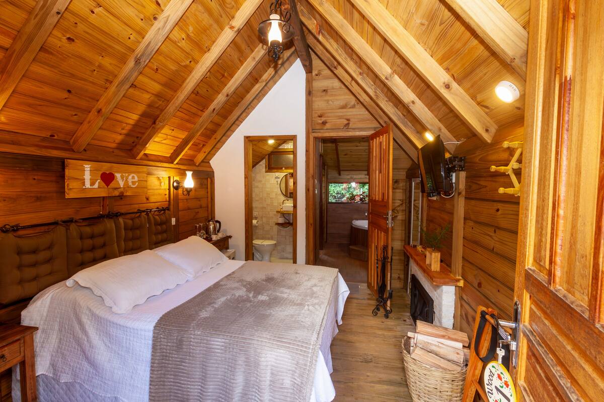 Quarto acolhedor de cabana de madeira, com cama, um letreiro com a palavra 'Love' e lareira.