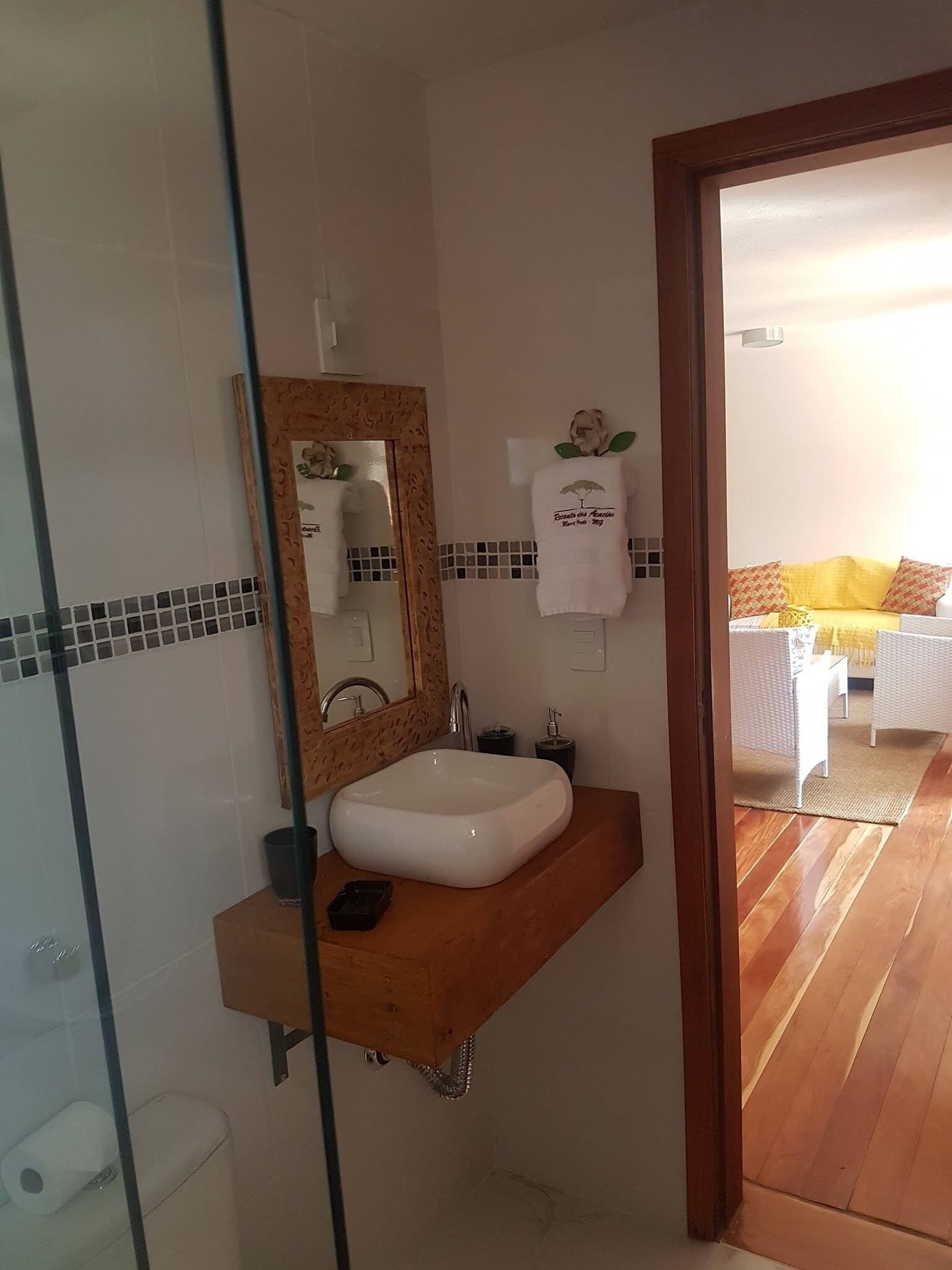 Un baño con un lavamanos blanco, un tocador de madera, un espejo con un marco decorativo y una toalla con un logotipo.