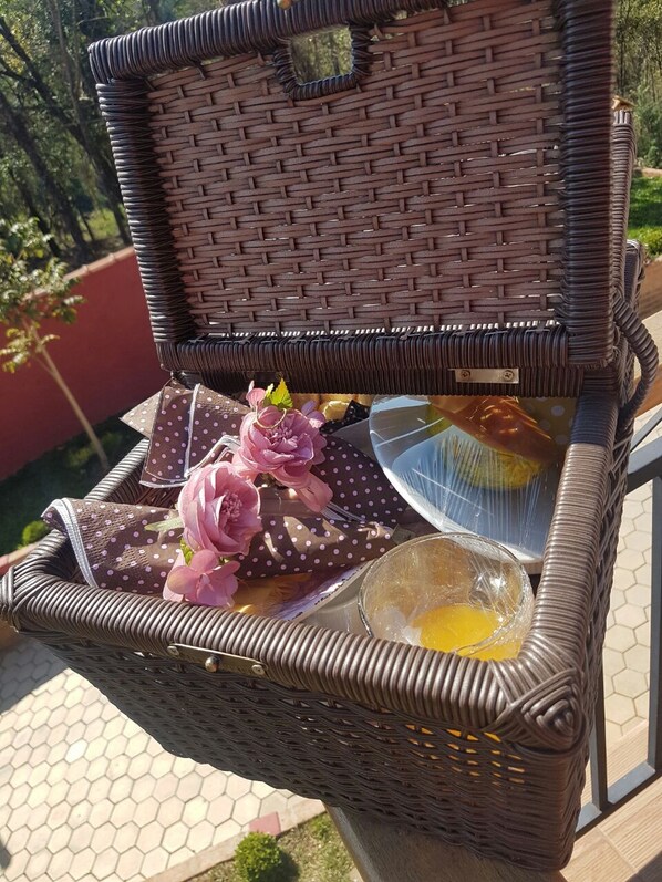 Una cesta de mimbre abierta con tapa, que contiene un paño con lunares, un cuenco de vidrio con un huevo y flores rosadas.