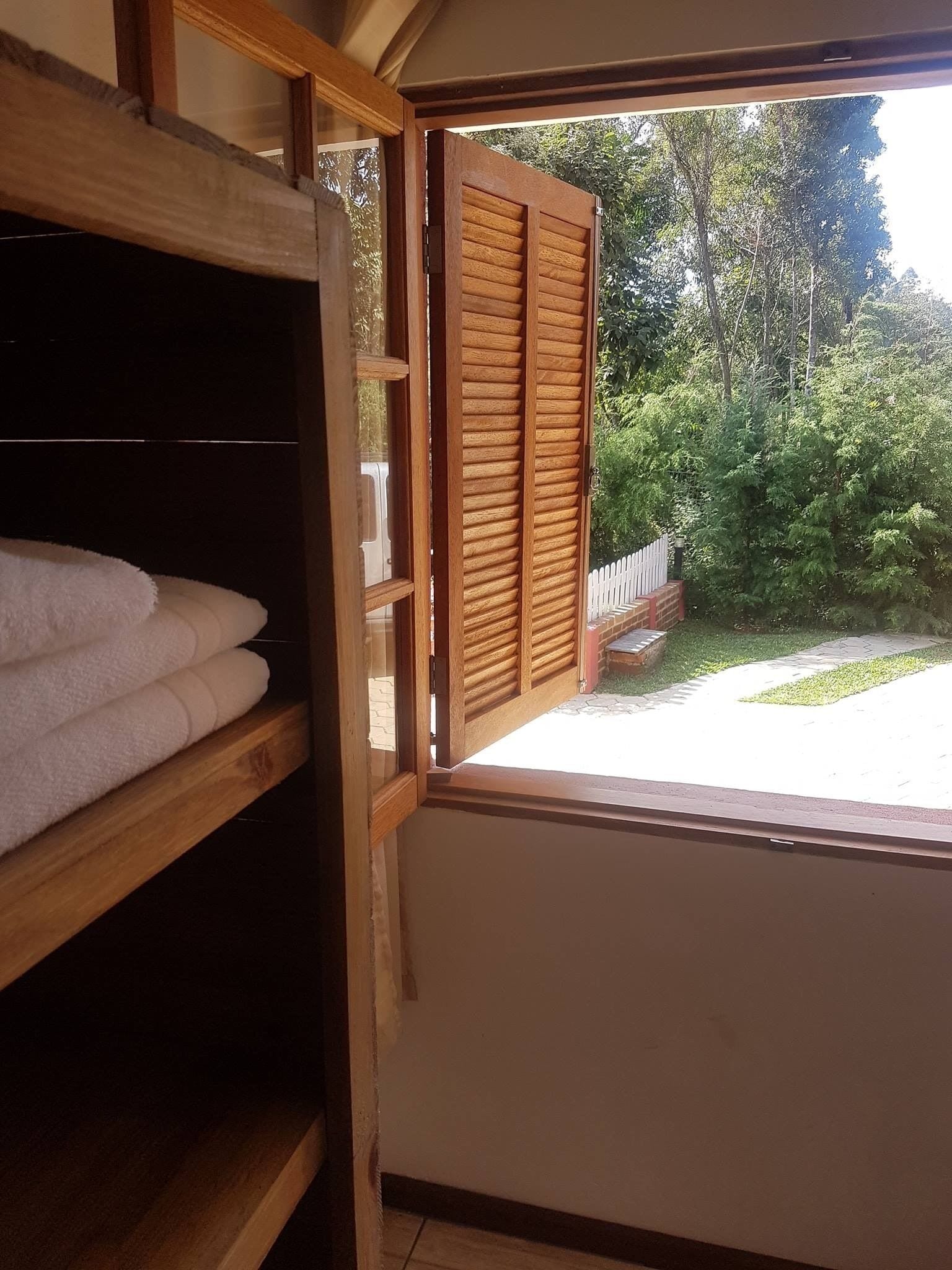 A room with a wooden shelf holding towels, a window with wooden shutters, and a view of a garden.