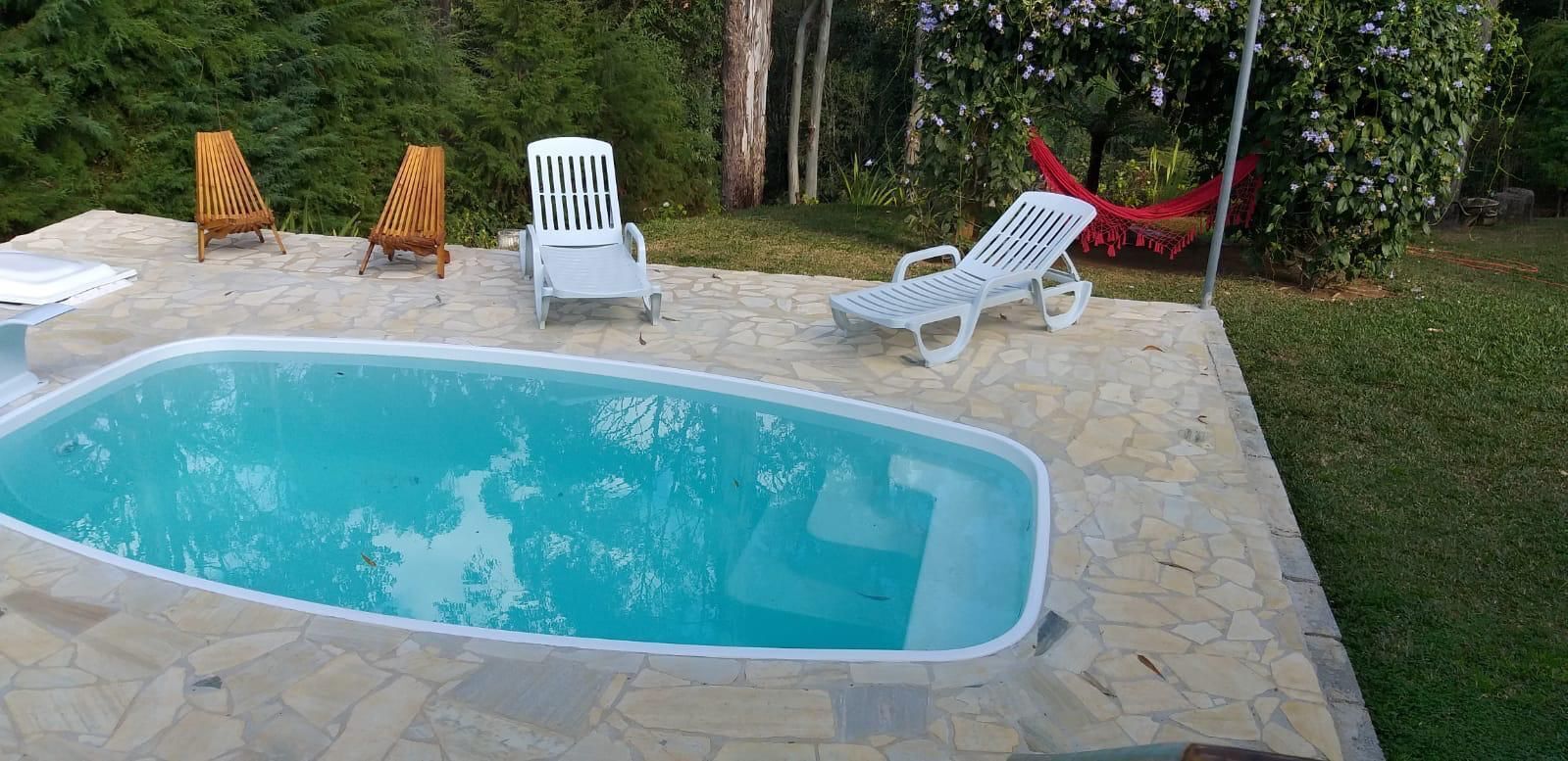 Una piscina con baldosas de piedra, rodeada de sillas de descanso y una hamaca.