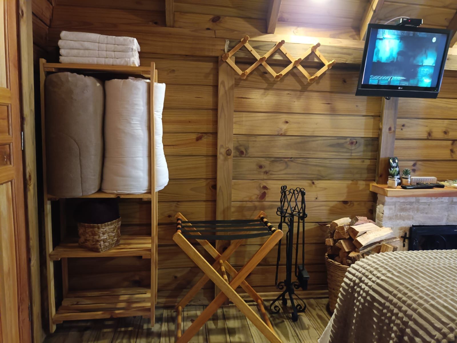 Interior acogedor de una cabaña con paredes de madera, una estantería con toallas dobladas, un tendedero, un televisor y una chimenea.