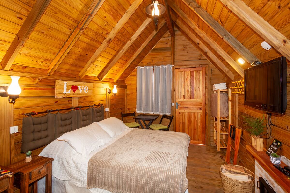 Um quarto acolhedor de cabana de madeira, com uma cama, uma televisão e uma pequena mesa.