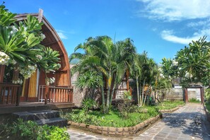 A wooden building with a curved roof, surrounded by lush greenery and palm trees. - GiliPaddy Resort (Gili Trawangan)