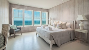 Ein Schlafzimmer mit einem großen Bett, zwei Nachttischen, einem Sessel und Meerblick durch große Fenster.