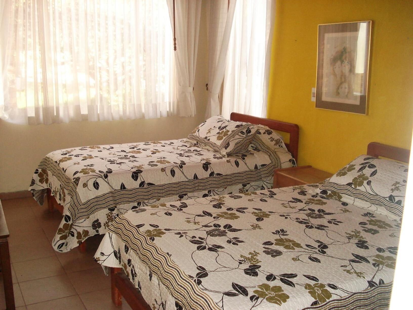 A room with two single beds, a window with sheer curtains, and a framed picture on the wall.