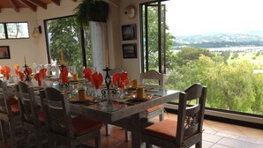 Comedor con mesa preparada para cuatro, sillas y vista a un paisaje verde a través de grandes ventanales.