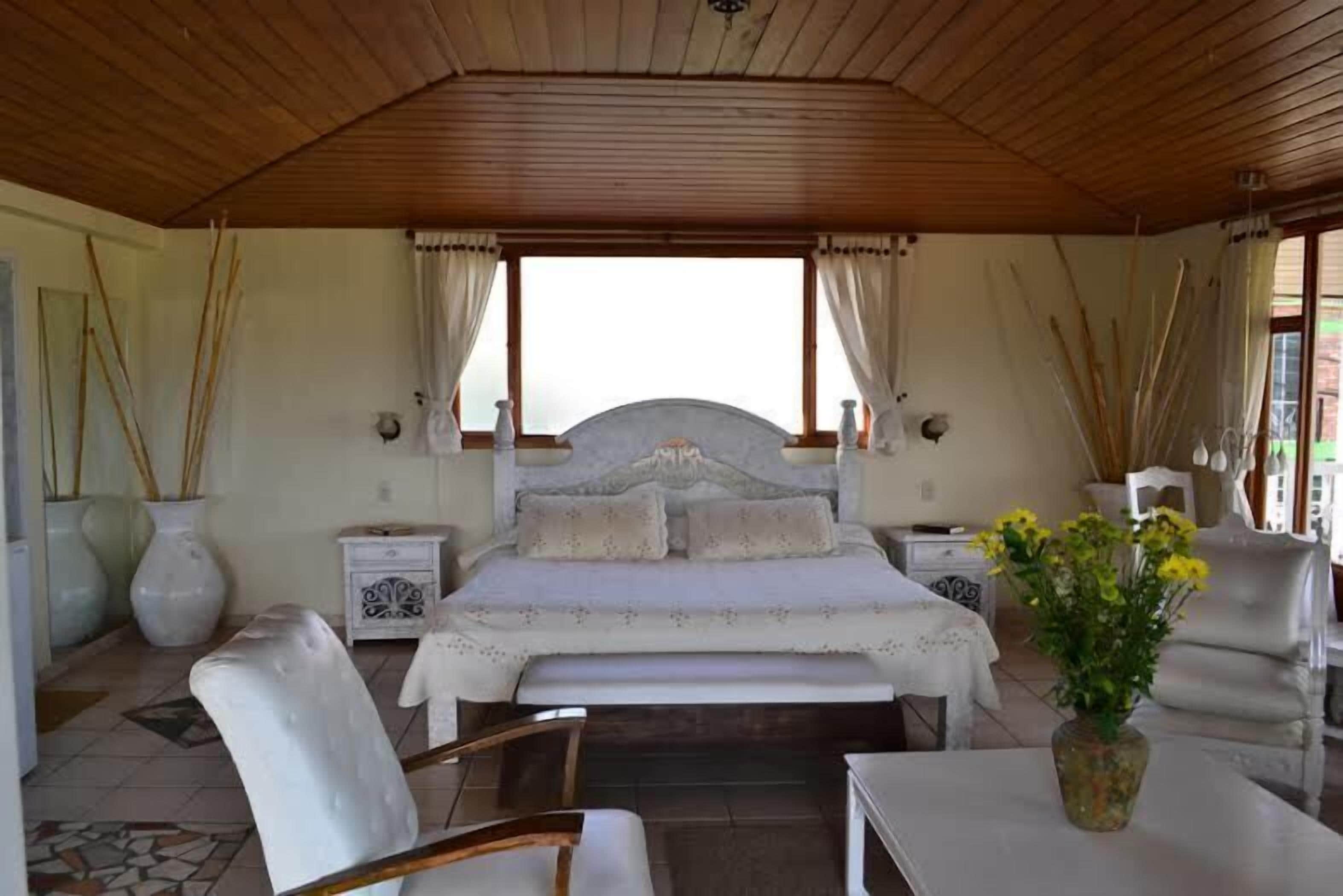 A bedroom with a large bed, two bedside tables, a chair, a small table, and a vase of flowers.